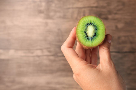 Woman holding delicious fresh kiwi on wooden background, closeup. Space for textの写真素材