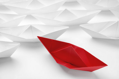 Red paper boat floating away from others on white background, closeup. uniqueness conceptの写真素材