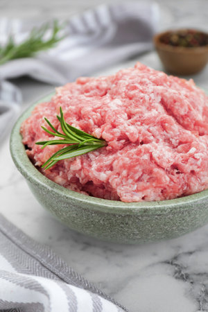 Bowl of raw fresh minced meat with rosemary on white marble table, closeup