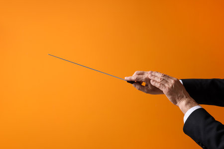 Professional conductor with baton on orange background, closeup. Space for textの写真素材