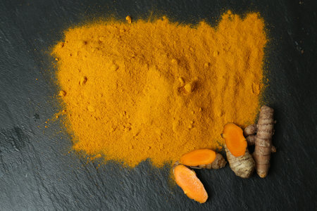 Turmeric powder and cut roots on black textured table, flat layの写真素材