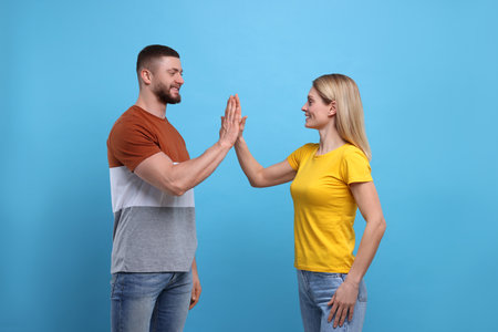 Happy couple giving high five on light blue background