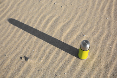 Yellow thermo with hot drink on sand, above view. Space for textの写真素材