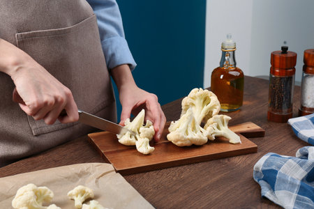 Woman cutting fresh cauliflower on wooden table, closeupの写真素材