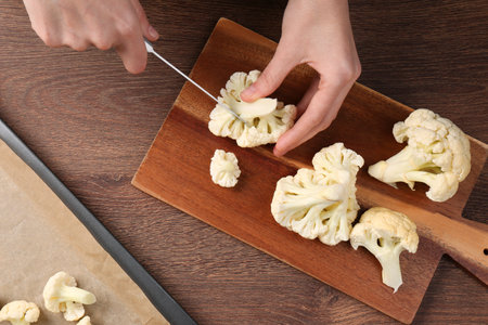 Woman cutting fresh cauliflower on wooden table, top viewの写真素材