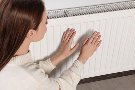 Woman warming hands on white heating radiator indoors, closeupの写真素材