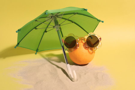 Funny orange with stylish sunglasses and umbrella on yellow backgroundの写真素材