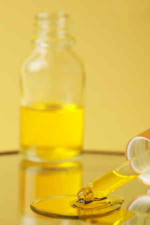 Dripping face serum from pipette on mirror against yellow backgroundの写真素材