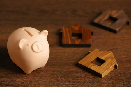 Piggy bank and house models on wooden table. Space for textの写真素材