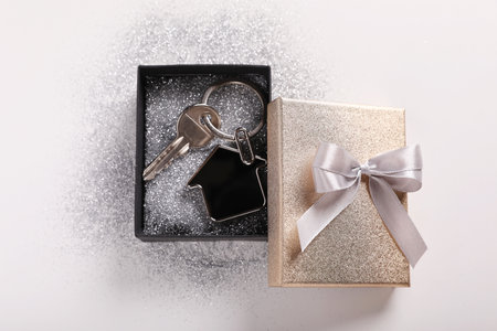 Key with trinket in shape of house, glitter and gift box on light gray background, flat lay. house warming partyの写真素材