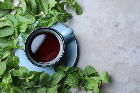 Cup with hot aromatic mint tea and fresh leaves on gray table, flat lay. Space for textの写真素材