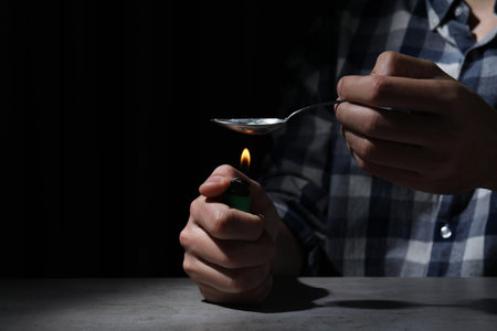 Man preparing drugs with spoon and lighter at gray table, closeup