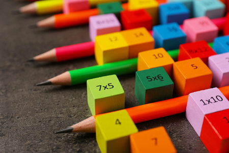 Many colorful cubes with numbers, multiplications and pencils on dark gray table, closeupの写真素材