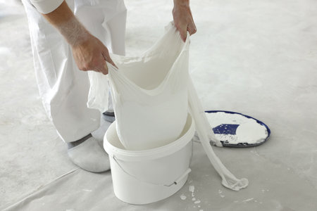 Decorator filtering paint in bucket on white floor, closeupの写真素材