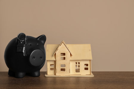 Piggy bank, keys and house model on wooden table against beige backgroundの写真素材