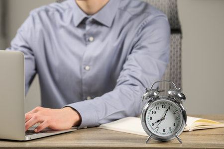 Silver alarm clock and man working at wooden table, closeup