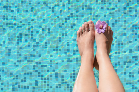 Woman with flower holding feet over water in swimming pool, closeup. Space for textの写真素材