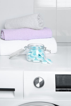 Jar with water softener tablets near stacked towels on washing machineの写真素材