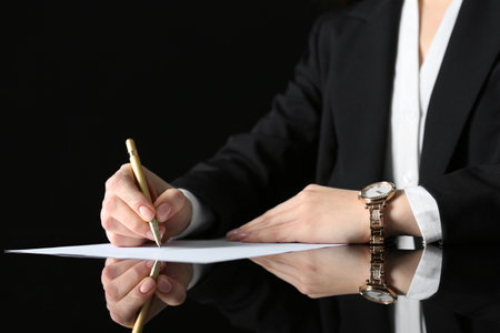 Woman writing on sheet of paper at glass table, closeupの写真素材
