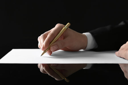 Woman writing with pen on sheet of paper at glass table, closeupの写真素材