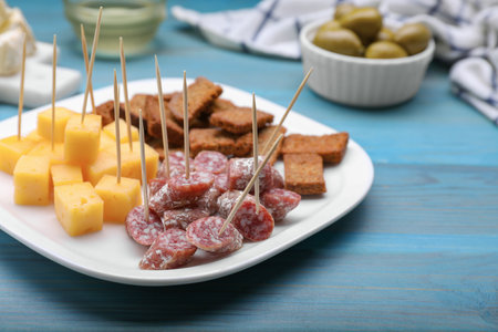 Toothpick appetizers. Pieces of sausage, cheese and croutons on light blue wooden table, closeup. Space for textの写真素材