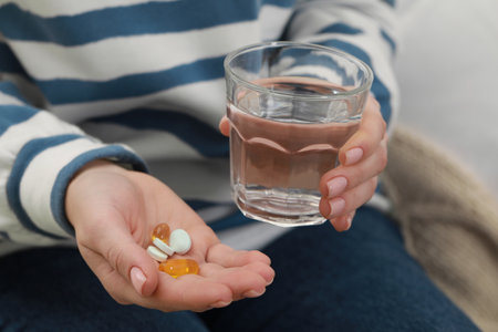 Woman with glass of water and pills indoors, closeupの写真素材