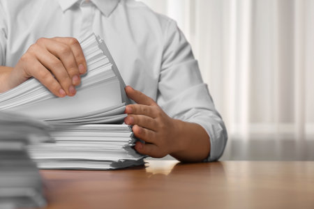 Man stacking documents at table in office, closeup. Space for textの写真素材