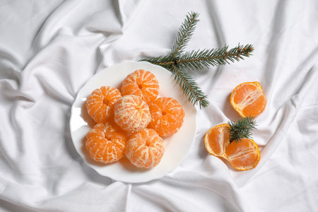 Peeled delicious ripe tangerines and fir branches on white bedsheet, flat layの写真素材