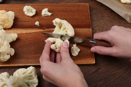 Woman cutting fresh cauliflower on wooden table, above viewの写真素材
