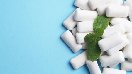 Tasty chewing gums and mint leaves on light blue background, flat lay. Space for textの写真素材