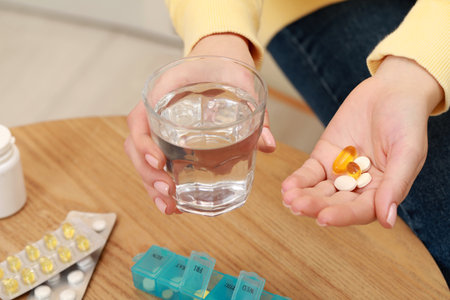 Woman holding glass of water and pills indoors, closeupの写真素材