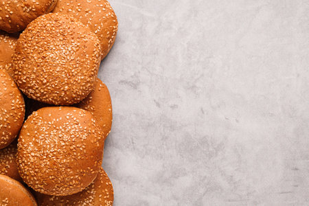 Fresh buns with sesame seeds on light gray table, flat lay. Space for text