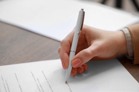 Woman signing documents at wooden table in office, closeup. Space for text
