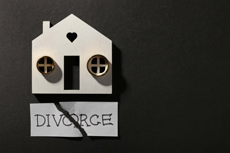 Pieces of torn card with word Divorce, wooden house and wedding rings on black background, flat lay. Space for textの写真素材