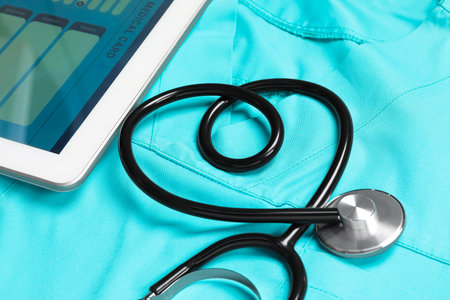 Stethoscope in shape of heart and tablet on turquoise medical uniform, closeupの写真素材