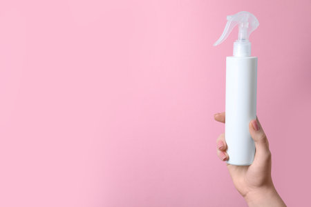 Woman holding spray bottle with thermal protection on light pink background, closeup. Space for textの写真素材
