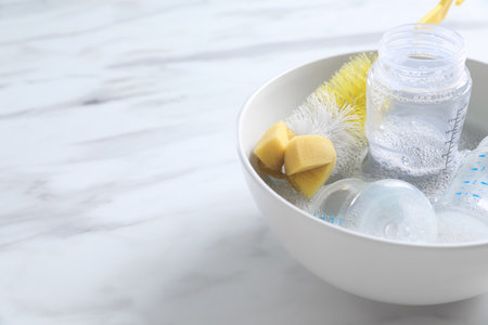Bowl with baby bottles and cleaning brush on white marble table in kitchen. Space for textの写真素材