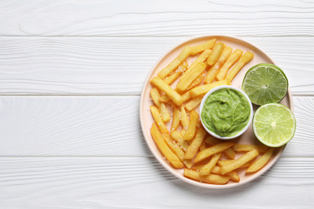 Plate with french fries, lime and avocado dip on white wooden table, top view. Space for textの写真素材