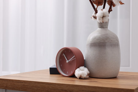 Alarm clock and vase with cotton branches on wooden table indoors. Space for text