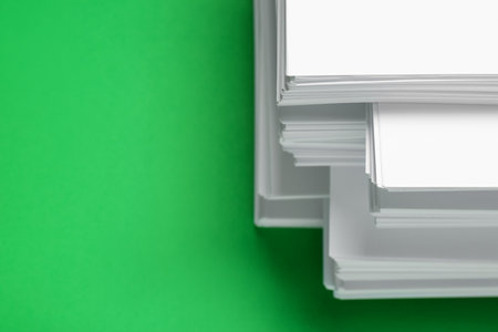 Stack of white paper on green background, closeup. Space for text