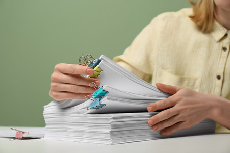 Woman stacking documents on white table against green background, closeup