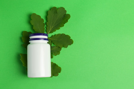 Medicine bottle and leaves on green background, top view. Space for textの写真素材