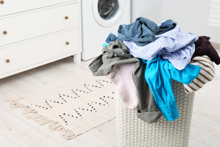 Plastic laundry basket overfilled with clothes in bathroomの写真素材