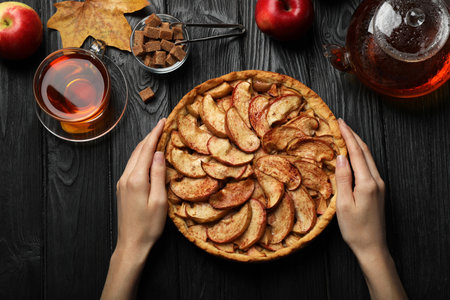 Woman with delicious apple pie at black wooden table, top viewの写真素材