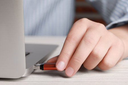 Woman attaching usb flash drive into laptop at wooden table, closeup