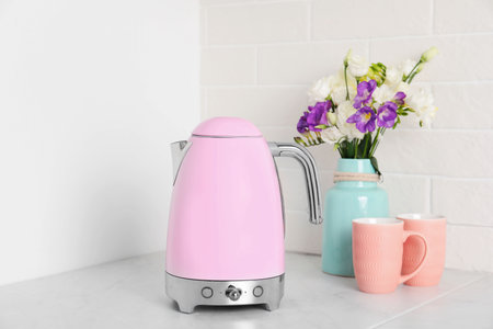 Modern electric kettle, bouquet and cups on counter in kitchenの写真素材