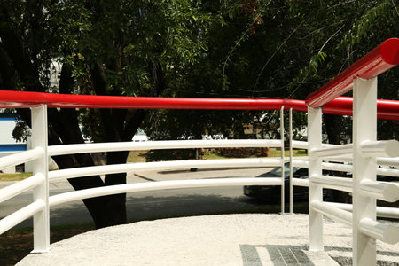 Ramp with red metal handrailings near trees outdoors