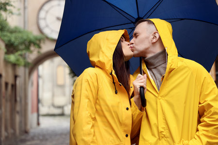 Lovely young couple with umbrella kissing under rain on city streetの写真素材