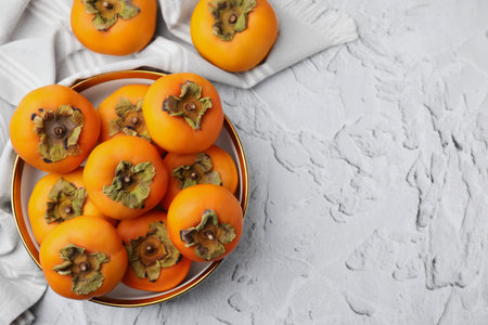 Bowl with delicious ripe juicy persimmons on white textured table, flat lay. Space for textの写真素材