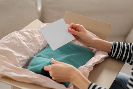 Woman holding greeting card near parcel with Christmas gift indoors, closeupの写真素材